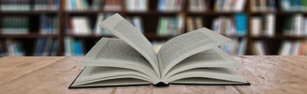 Open book on wooden table in a library with bookshelves in the background, representing LS Lane Books' extensive collection of literature and educational resources.