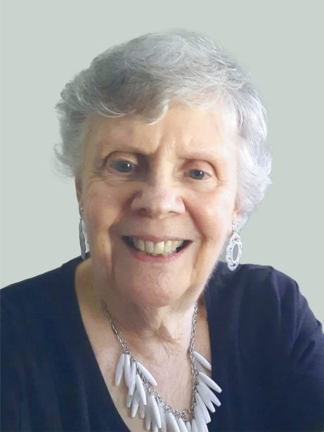 Smiling elderly woman with short gray hair wearing white jewelry and a black top, close-up portrait, cheerful expression, friendly appearance, modern photo, light background.
