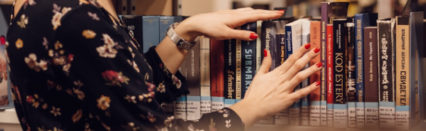 A woman's hands stroke the book covers in a bookshelf as she decides what to read next.